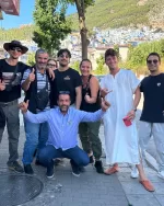 Group of eight friends posing for a photo on a sunny street with a hillside town in the background.