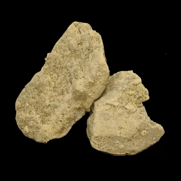 Cluster of rough, light‑beige rocks with a granular surface against a black background.