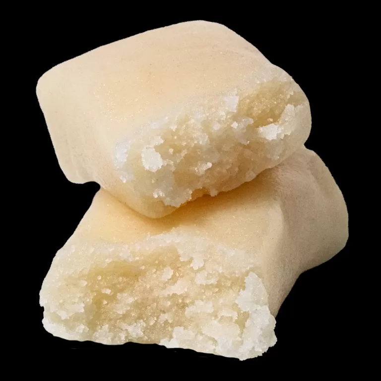 Close-up of a pale beige mineral with white crystalline patches on a black background, showing a curved edge.