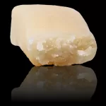 Beige irregular rock with white mineral patches on a black background.