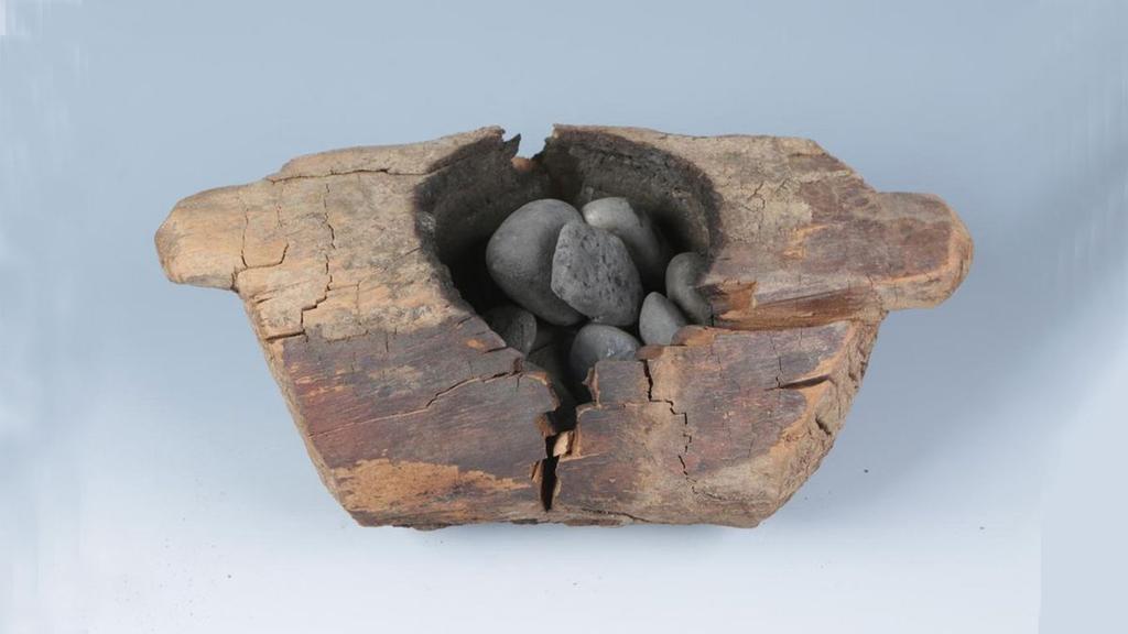 Cracked, weathered wood with smooth gray stones nestled inside a hollow.